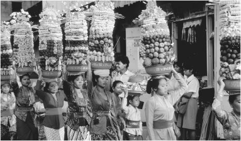 Women carry towering baskets of fruit on their heads for a temple festival in Bali.