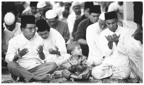 A young boy watches the adults as they perform the noon prayer at a  mosque in Bandar Seri, Begawan. The Shafeite sect of Islam is the  national religion.