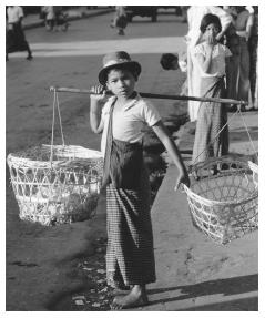 A child carrying baskets on a shoulder pole. Traditionally, all boys of eight to ten years of age attended school in a Buddhist monastery.