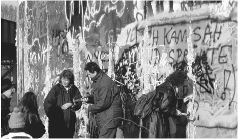 People collecting pieces of the Berlin Wall in 1989. Built in 1961, the wall was a visible reminder of Germany's defeat in World War II and subsequent division into first four, then two distinct and independent zones.