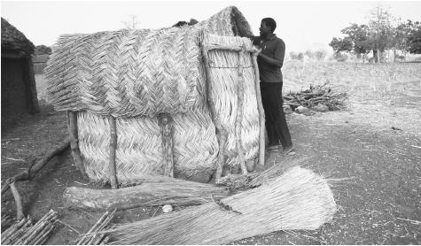 A man builds a small granary from wood and straw for his village in Ghana. The country's economy is primarily agricultural.