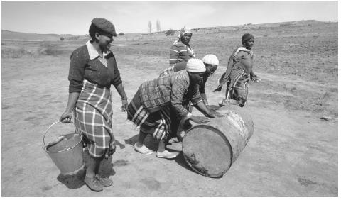 Women roll barrels and carry buckets containing materials needed for the construction of a reservoir.