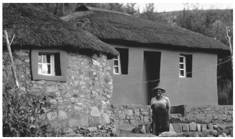 A woman standing by a row of thatched houses. Over 80 percent of Lesotho's population lives in the country's lowland area.