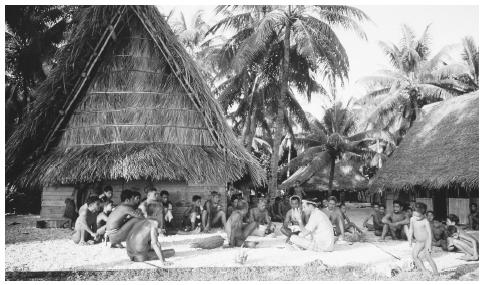Men gather for a meeting outside the men's house, a community building where men eat, sleep, and store their canoes. Meetinghouses and feast houses are important places for social interaction among Micronesians.