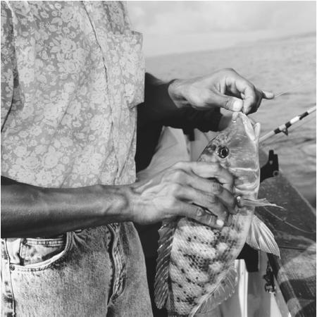 A man holds a green fish he caught using Daiwa tackle. A subsistence economy of farming and fishing remains fundamental.