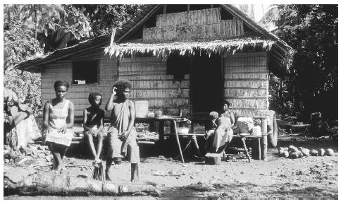 A family relaxes on benches in front of their house in Falamai Village. Stilts and windows provide needed ventilation in the equatorial climate.