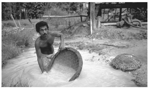 Wading in a pool of brackish water, a man pans for rubies, sapphires and other gems using a basket at one of Sri Lanka's many pit mines.
