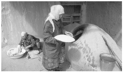 A woman places flat bread dough in an oven, while another woman folds dough in a large bowl, Old Town, Khiva. Families are patriarchal, but mothers run the households.
