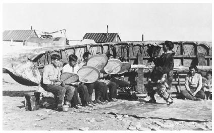 Inuit men in Nome, Alaska play drums and sing as another man dances.