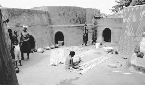 Painted huts enclose a courtyard where a woman weaves mats from millet stalks. Such courtyards serve as the primary focus of domestic activity.